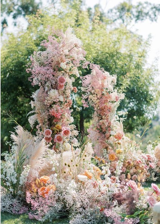 a fantastic and super lush wedding arch with pink, yellow and orange blooms and blooming branches plus pink baby's breath all over
