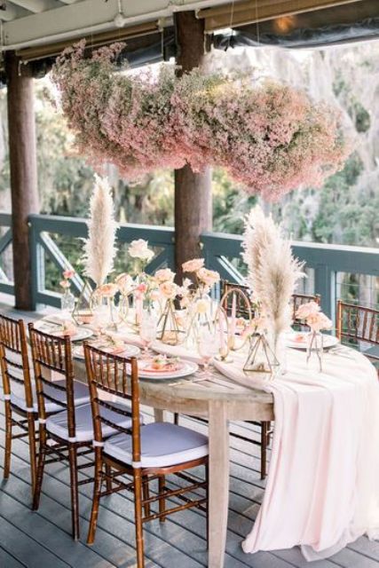 a beautiful and dreamy boho wedding tablescape with pink roses and pampas grass plus a pink baby's breath installation over it