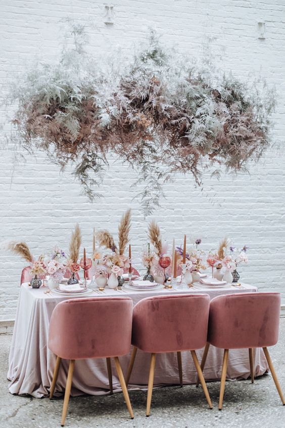 a rose-inspired wedding reception space with pampas grass, touches of pink and a pale greenery and blush floral and greenery installation over the table