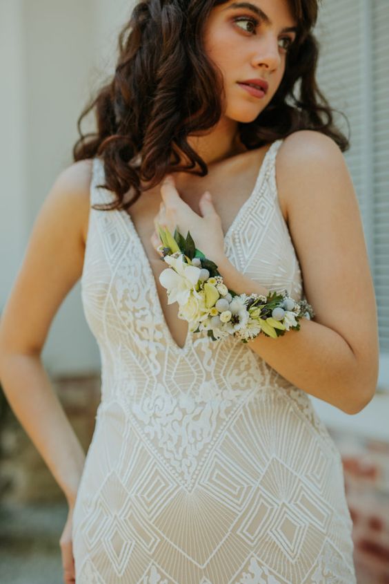 a catchy tan and white lace fitting wedding dress with a covered plunging neckline and a long neutral flower bracelet wrapping the arm