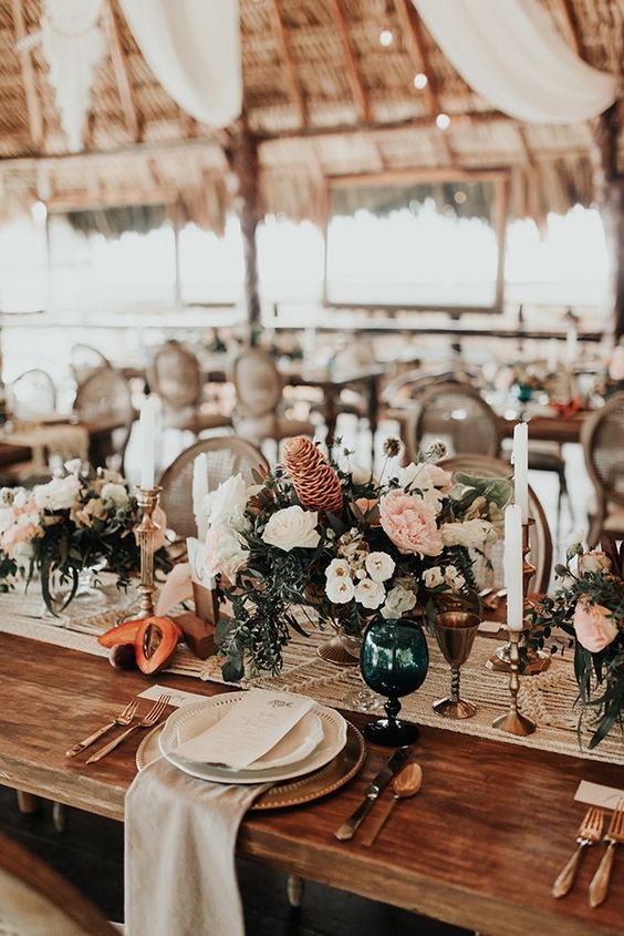 a beach boho wedding tablescape with a macrame table runner, fruits, lush florals, candles and a neutral napkin
