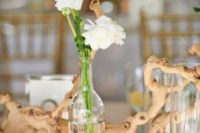 a beach wedding centerpiece of driftwood, white blooms in a bottle and candles in glass candleholders