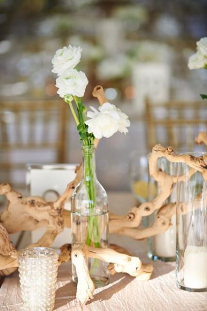 a beach wedding centerpiece of driftwood, white blooms in a bottle and candles in glass candleholders