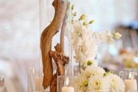 a beach wedding centerpiece of white blooms, seashells, candles and driftwood in a tall jar looks spectacular