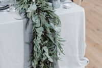 a beautiful greenery wedding table runners of various kinds of eucalyptus, with a grey runner and candles