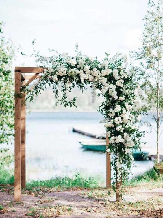 a beautiful wedding arch of wood, with lush greenery and lots of white blooms is rustic classics to try for a backyard wedding