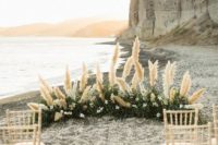 a boho beach wedding altar with greenery, white blooms and pampas grass plus simple chairs
