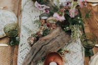 a boho beach wedding centerpiece of driftwood, greenery, pink blooms, candles and a macrame runner