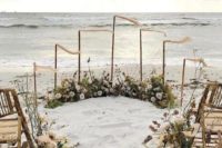 a boho beach wedding ceremony space done with lots of dried blooms, white and blush florals, flags and wicker chairs
