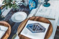 a boho chic tablescape with a tie dye table runner, blue glasses and agates, wooden chargers and blooms