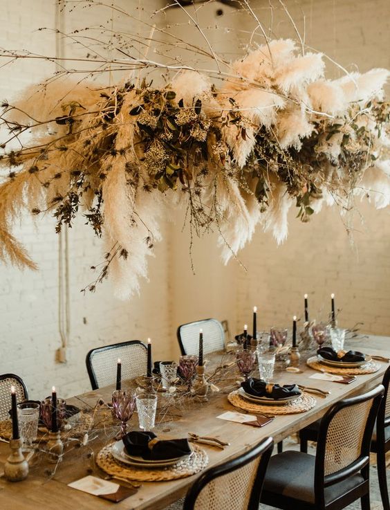 a boho chic tablescape with black napkins and candles, wicker chargers, geometric touches, dried florals and pampas grass