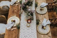 a boho chic wedding table setting with a macrame table runner, dyed napkins, lush florals and greenery, gilded plates and candles