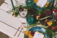 a boho gypsy tablescape with bright green and turquoise plates, colorful glasses and candles and lush florals and greenery