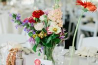 a boho summer wedding centerpiece with air plants, bright blooms, a monstera leaf and bottles and vases