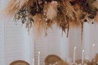 a boho tablescape done with gilded leaves, brown menus and neutral napkins plus an oversized dried floral and herbs installation