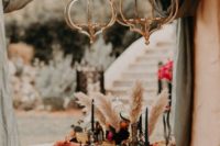 a boho tablescape with a velvet and tie dye runner, black candles, colored glasses, colorful napkins and pampas grass