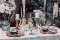a boho tablescape with a whitewashed table, macrame placemats, colored glasses, candles and florals