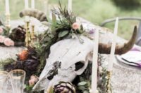 a boho wedding centerpiece with greenery, artichokes, blush blooms, candles and a large skull