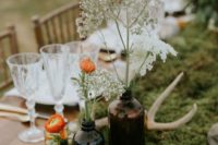 a boho wedding centerpiece with moss, apothecary bottles with blooms and wildflowers and candles