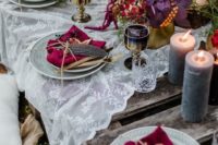 a bright boho meets decadent tablescape with candles, a lace tablecloth, colorful napkins, feathers, greenery and blooms in supmtuous colors