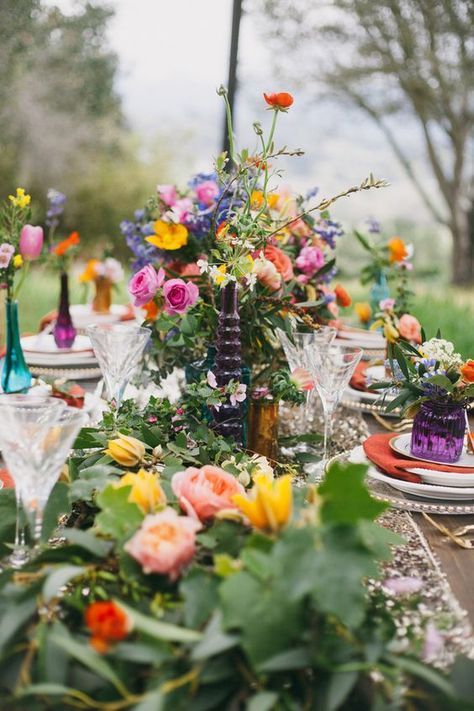 a bright boho spring bridal shower table with greenery, colorful flowers, colorful glasses and vases