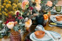 a bright boho wedding tablescape with blue plates and chargers, bowls, lush florals and colored glasses