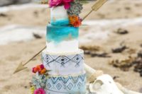 a bright turquoise wedding cake with tribal patterns, ombre, gold leaf, bright blooms and succulents and a large arrow