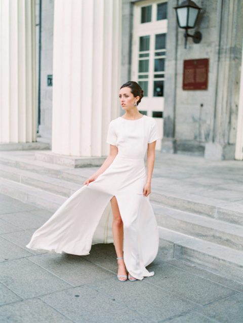 a casual plain maxi wedding dress with short sleeves, a high neckline, a front slit and blue heels plus statement earrings
