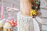 a catchy boho wedding cake with an ikat tier and a sugar macrame one plus some feathers with gold edges and sugar berries and leaves