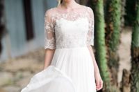 a chic empire waist wedding dress with a pleated skirt and a sheer lace and embellished coverup with short sleeves