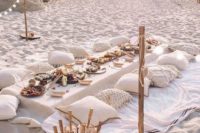 a chic neuutral boho beach picnic setting with crochet pillows, a white tablecloth and lots of food