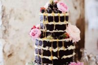 a chocolate wedding cake with honey drip, fresh blooms and greenery and berries on top for a summer boho wedding
