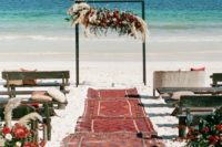 a colorful boho beach ceremony space with boho rugs, colorful blooms, greenery, pampas grass and an oversized floral installation