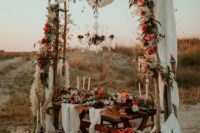 a colorful boho beach wedding reception space with colorful blooms and pampas grass, a crystal chandeliet, airy runners and lots of candles