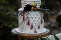 a creative wedding cake with sugar macrame decor and dip dyed tassels plus greenery and little apples for a boho wedding