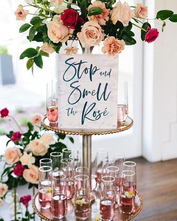 a cute and elegant rose bar with drinks with petals, lush blooms and a simple and cute sign
