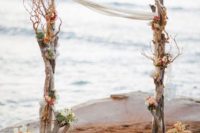 a driftwood wedding arch with peach and white blooms, seashells and succulents plus candle lanterns