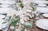 a driftwood wedding centerpiece with greenery, seashells, succulents and white blooms is timeless for a beach wedding