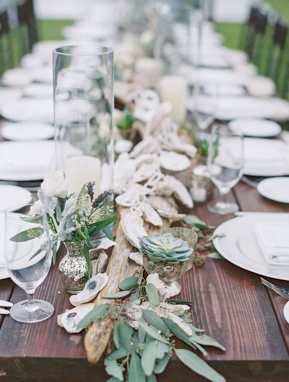 a driftwood wedding centerpiece with greenery, seashells, succulents and white blooms is timeless for a beach wedding