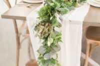 a fern and eucalyptus wedding table runner combined with a white fabric one and spruced up with gold candle holders