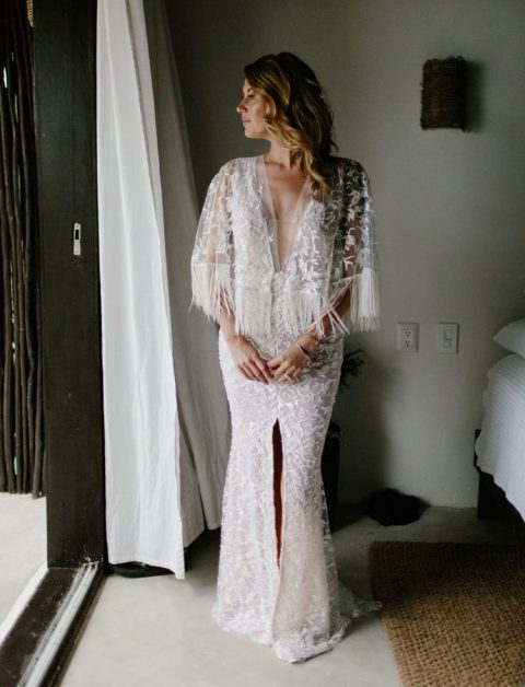 a glam boho gown with lace appliques, a plunging neckline, a front slit and long fringe on the bell sleeves