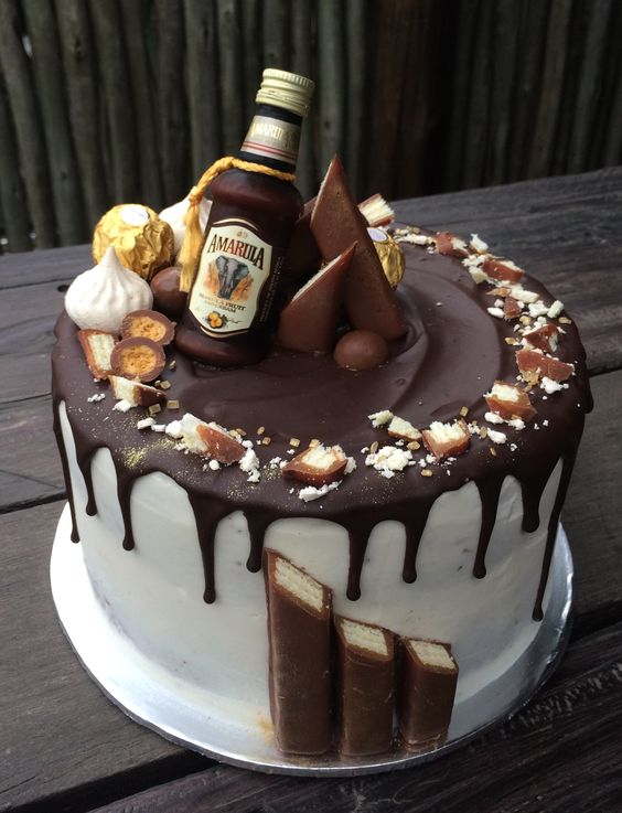 a gorgeous groom's cake with chocolate drip, nuts, meringues, caramel and a chocolate alcohol bottle is a great and tasty solution