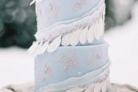 a light blue wedding cake with sugar beads, ribbons with beads and white feathers is a gorgeous idea for a winter boho wedding
