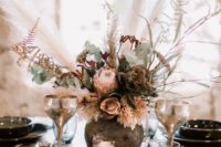 a lush boho wedding centerpiece with pink and mauve blooms, greenery, herbs and pampas grass