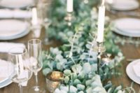 a lush eucalyptus table runner with mercury glass candle holders and metallic holders looks chic