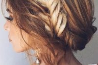 a messy and wavy updo with a large fishtail braid in the center and locks down