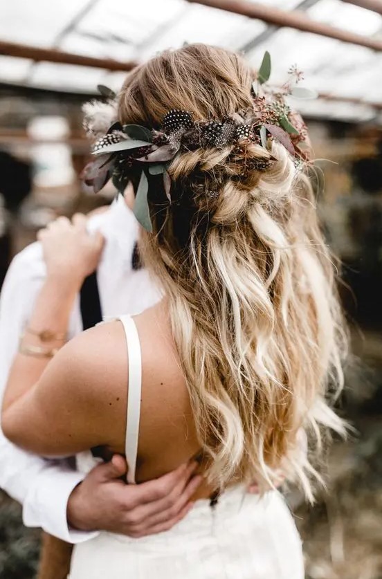 a messy textural half updo with twists and braids and greenery and feathers
