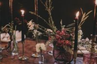 a moody boho wedding centerpiece with white and bright blooms and herbs plus black candles