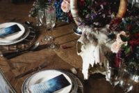a moody boho wedding tablescape with patterned plates, an animal skull, lush florals, candles and greenery