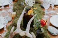 a moss table runner, antlers, bottles with bright blooms and candles plus neutral plates and glasses
